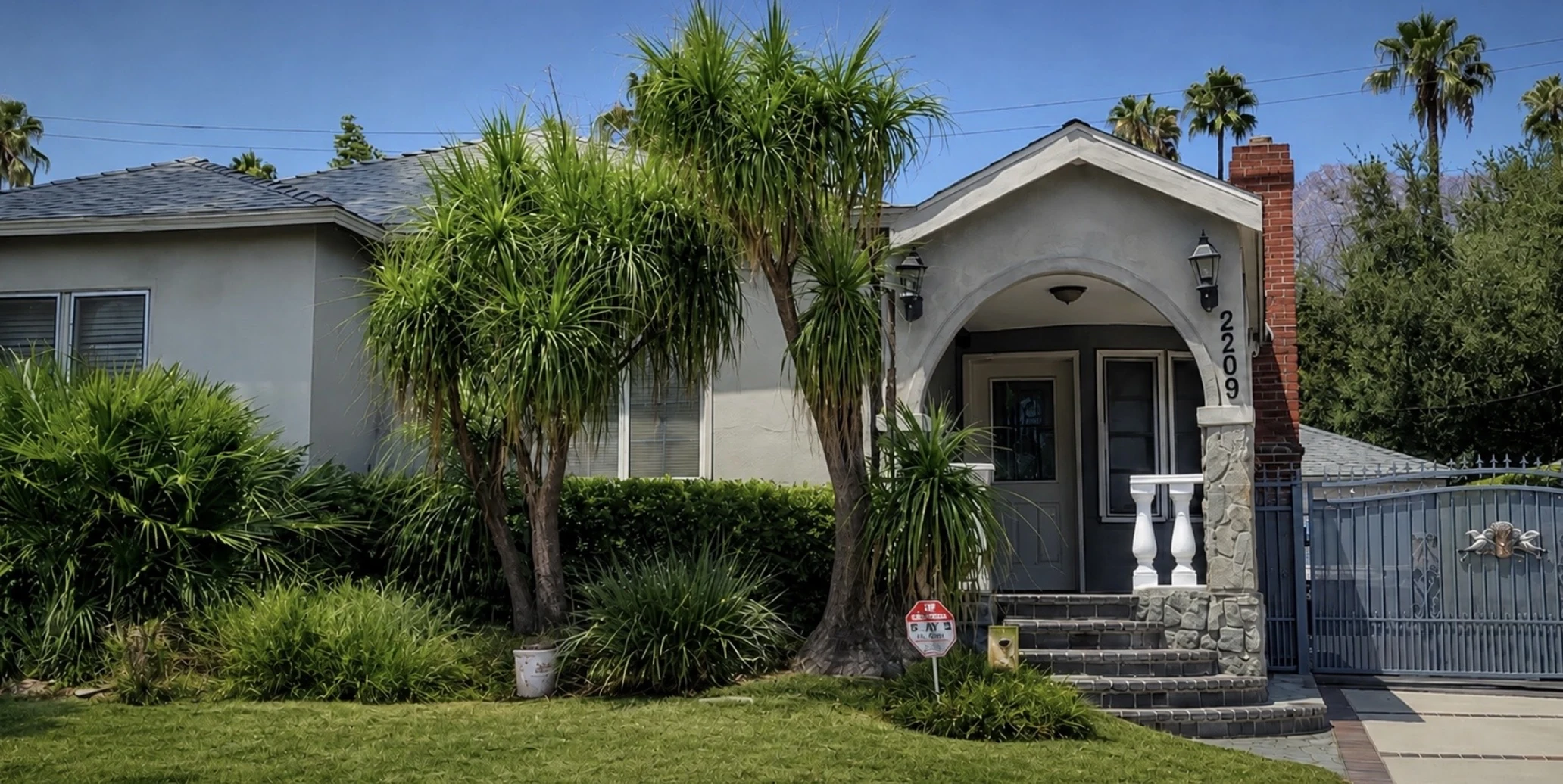 2209 Queensberry Road, Pasadena, CA 91104 的正面外观,可见拱形门廊入口、石柱上的2209门牌号以及带门的车道
